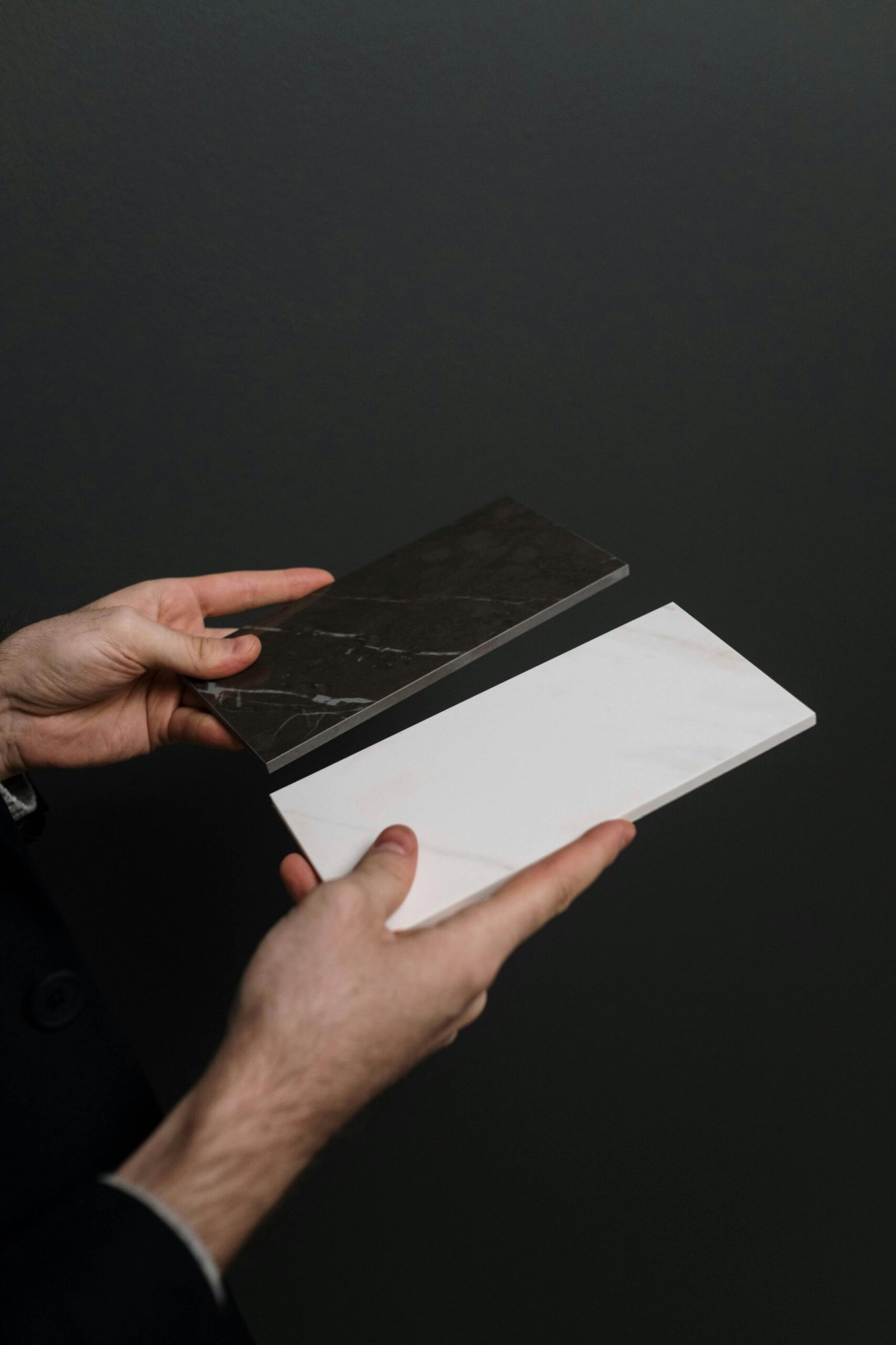 Close-up of hands holding elegant black and white marble tiles against a dark background.
