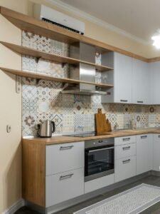 Modern kitchen with electric appliances and radiator against table with tasty biscuits and cups illuminated by bright chandelier