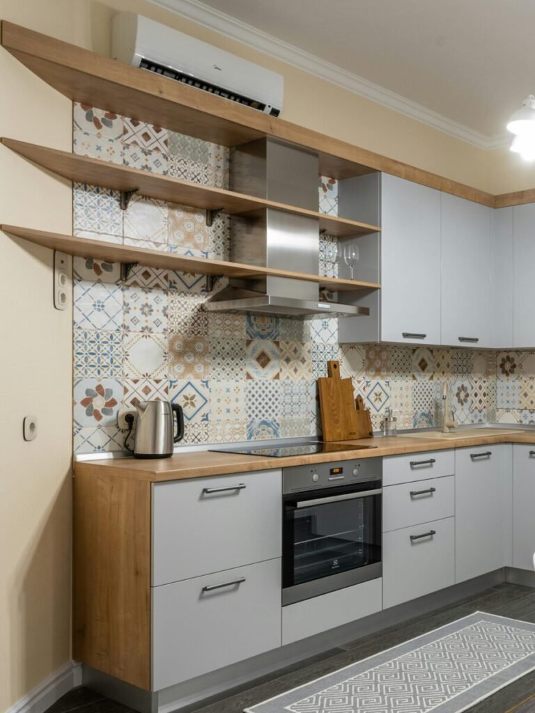 Modern kitchen with electric appliances and radiator against table with tasty biscuits and cups illuminated by bright chandelier