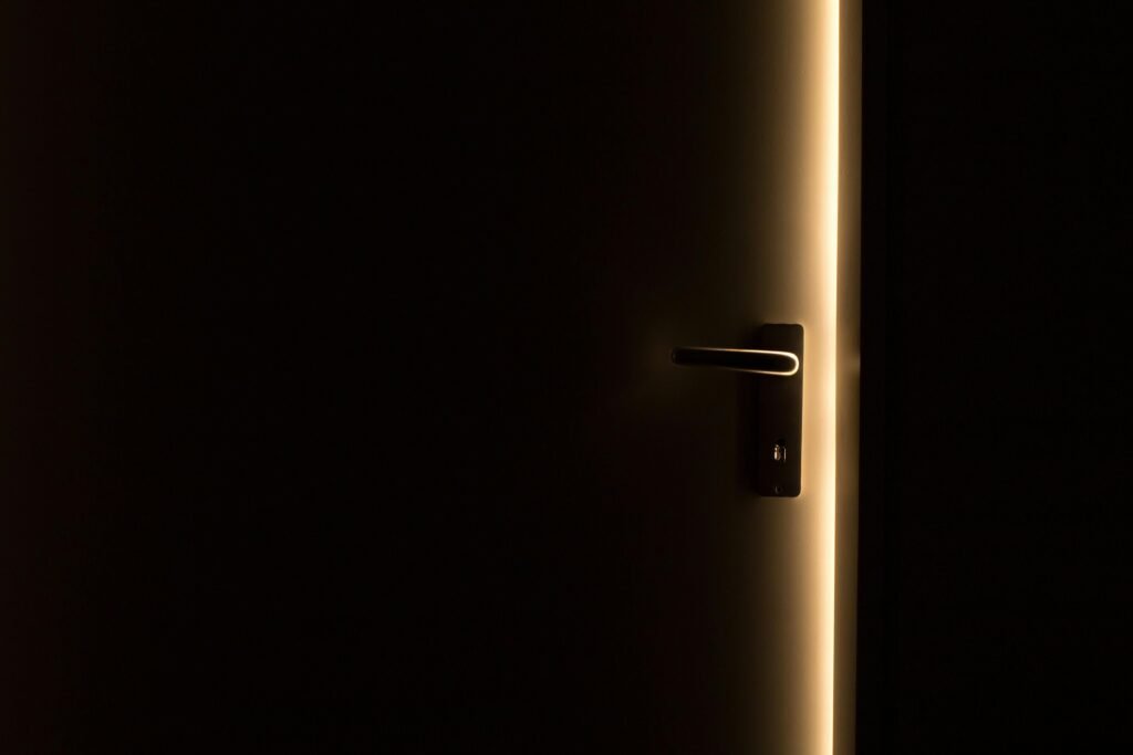 A dark room with a door slightly ajar, revealing a glowing light through the opening.