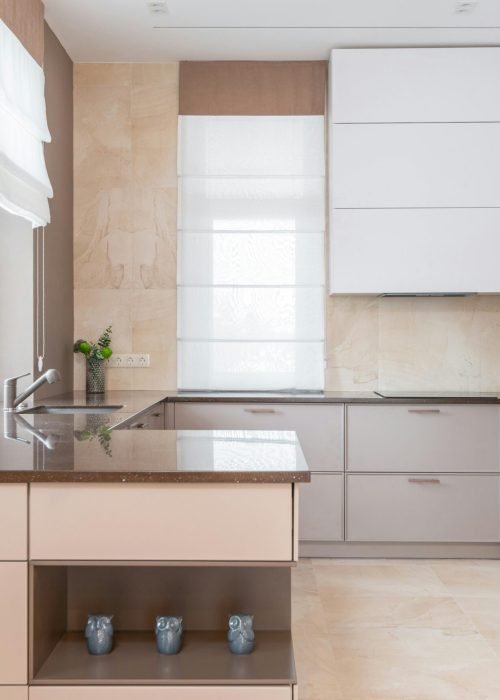 Home Empty contemporary kitchen with beige walls and light floor tile furnished with minimalist cupboards with gray panels equipped with oven and built in appliances